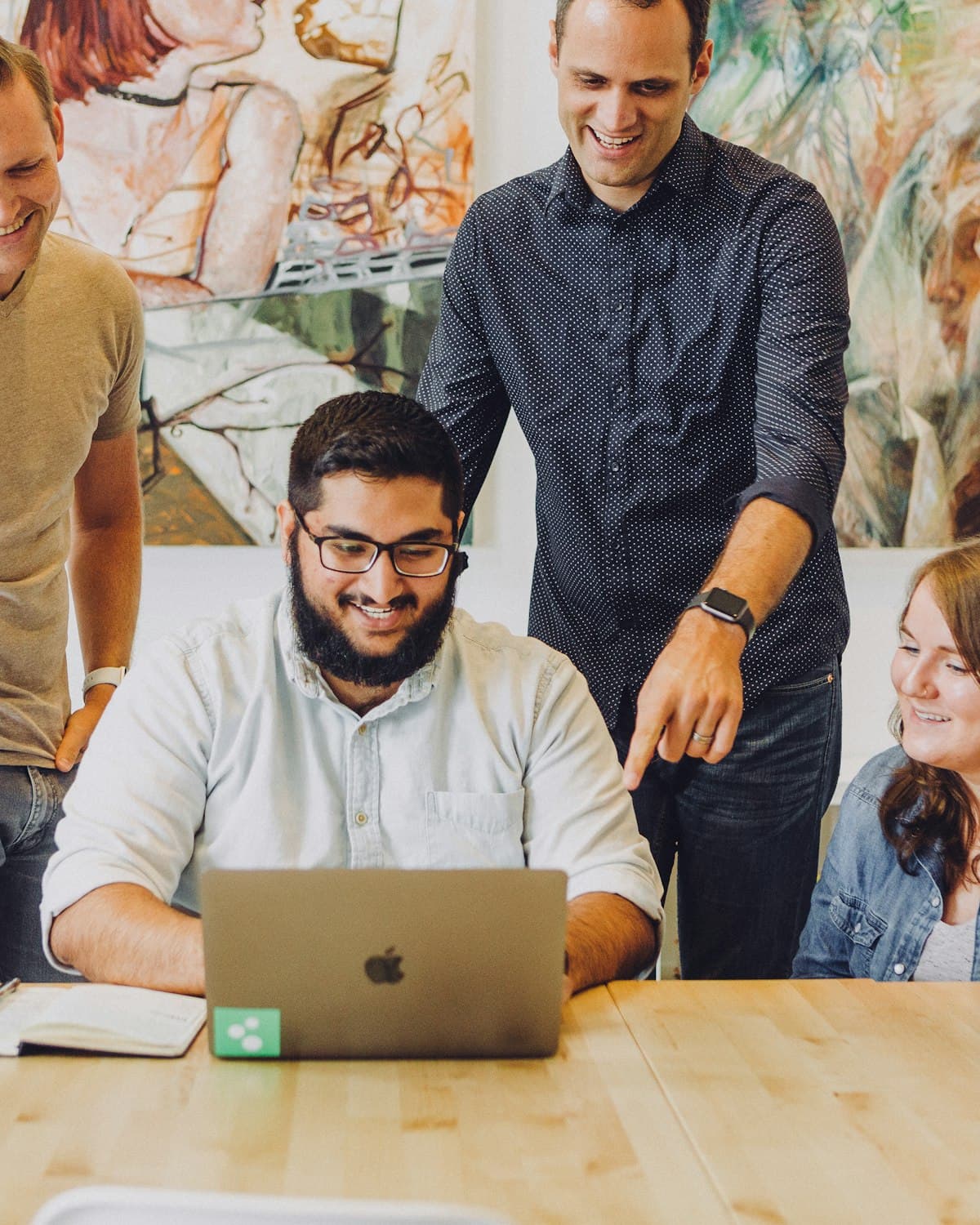 Four colleagues smiling around a laptop